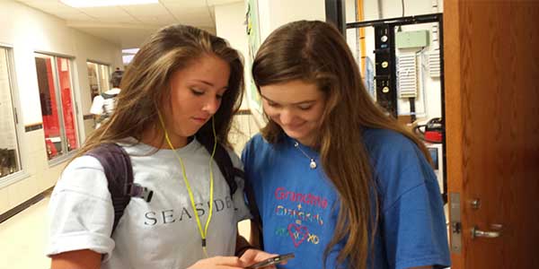 The schools new policy will prevent students such as sophomore Mady Daddario, looking at her phone with fellow sophomore Keegan Williams, from wearing earbuds in both ears while in the schools common areas such as the hallways.