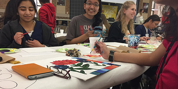 Senior Sara Ahmed paints a canvas with a colorful flower. 