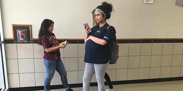 Talking with friends sophomore Melika Delkaninia rests her arm on her fake pregnant belly as part of a project in her Child Development class. 