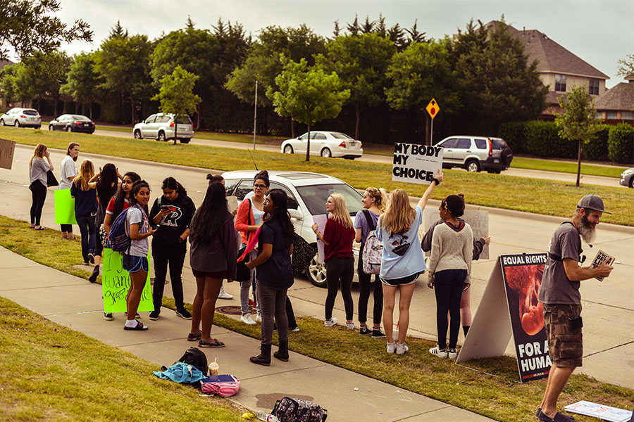 With a line of cars waiting to turn into the schools main entrance, students protest in front of the school on the morning of Thursday, May 18, 2017. 