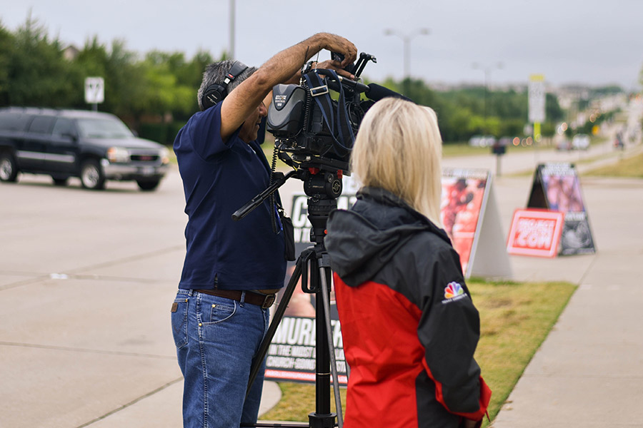 NBC 5 videographer Roy Hernandez adjusts his equipment as reporter Lexie Houghtaling stands to his side waiting to do an interview Tuesday, May 23, 2017. 