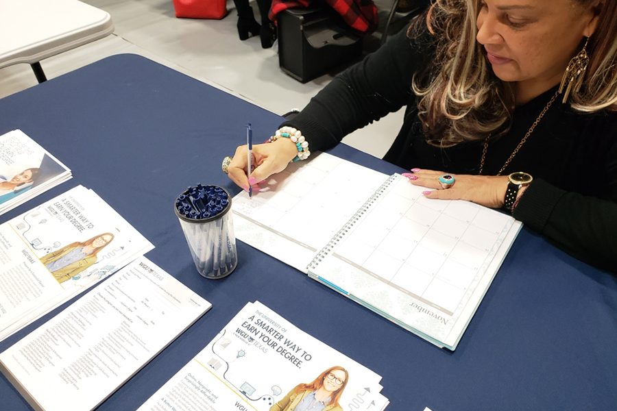 Representative for Western Governors University, Barbera LeCesne, writes down upcoming dates in her planner as she waits for students to arrive at her college informational table.
