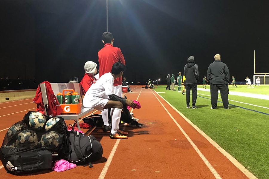 While boys soccer battles against the Lions on the field, Redhawks teammates watch from the bench on Friday, Jan. 18.