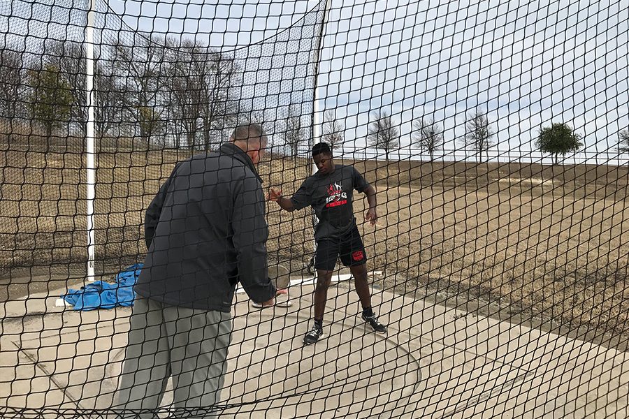 Demonstrating how to hold the discus, coach Chris Burtch works with sophomore Prince Ugoh, a sophomore, on the back practice fields.  On Friday, members of the track team will head to Denton to compete in the Wildcat Relays. 