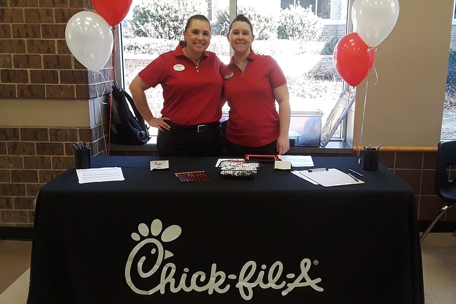 Two managers from Chick-fil-A pose in front of their table in the cafeteria. They hope that they can recruit new employees. “Its really, really important to start work ethic very, very young, you have to work to earn bread and a house and all of those things and so you might as well love what you do,” manager Kasey Sjoerdsma said. 