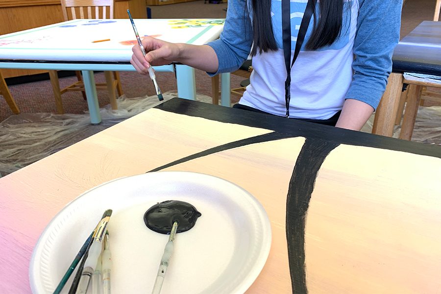 Sophomore Kimberly Nguyen, paints a second coat of black paint onto the library table. The second coat is needed to create a smoother and less translucent look to the design.
