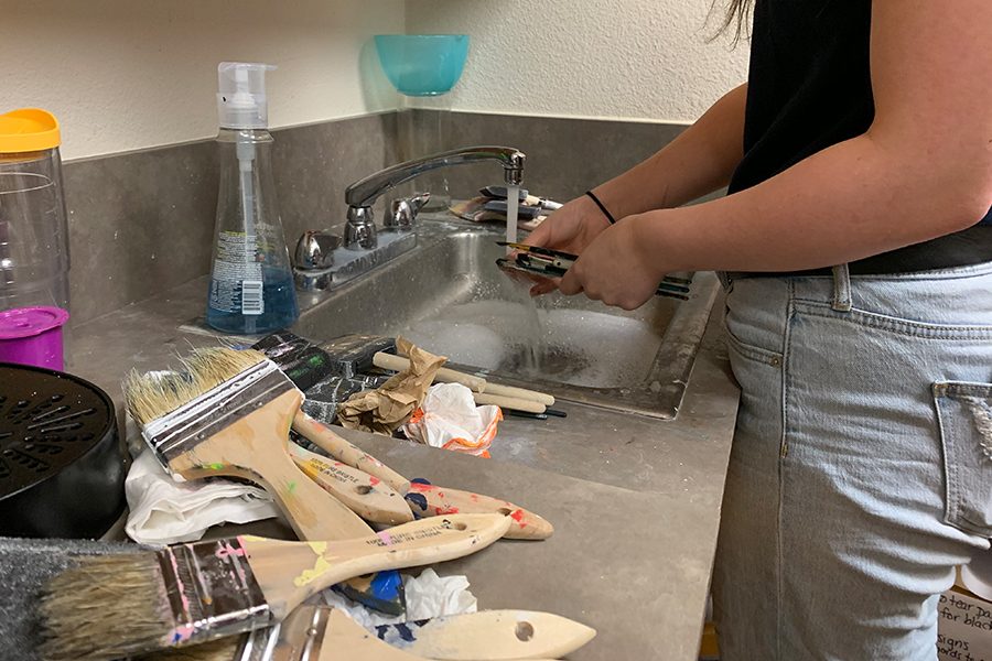 After painting the library tables, Junior Raina Kinneer, washes the paint covered brushes in the library office sink. There is a large pile of wet paint brushes next to the sink that continue to sry from previous students use.  