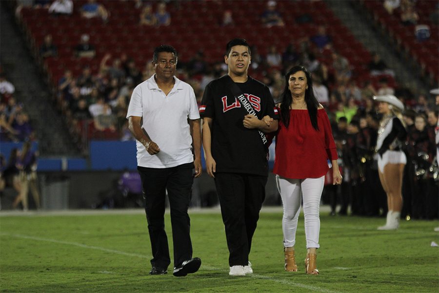 Homecoming King winner Andres Venegas walks across the field with his parents Jimmy Venegas and Maria Bustos during the announcement of the Homecoming Court on Thursday during halftime of the football game at Toyota Stadium. 
 