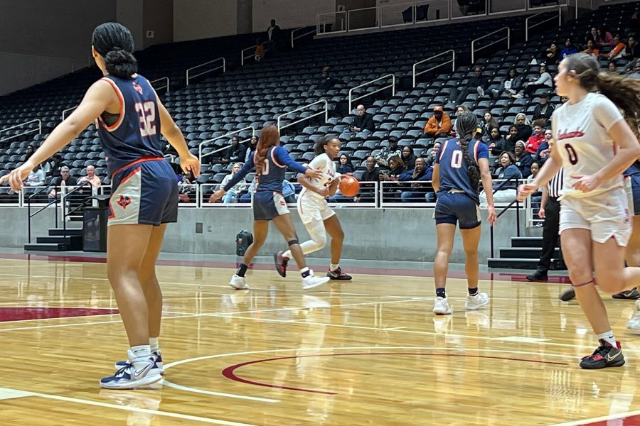 As senior Jezelle Jolie Moreno cuts through the lane, freshman Jacy Abii dribbles outside the 3-point line during the Redhawks 5A Regional final on Saturday in Garland. Abii would kick start the Redhawks in the first half, scoring 10 of her 12 points. 