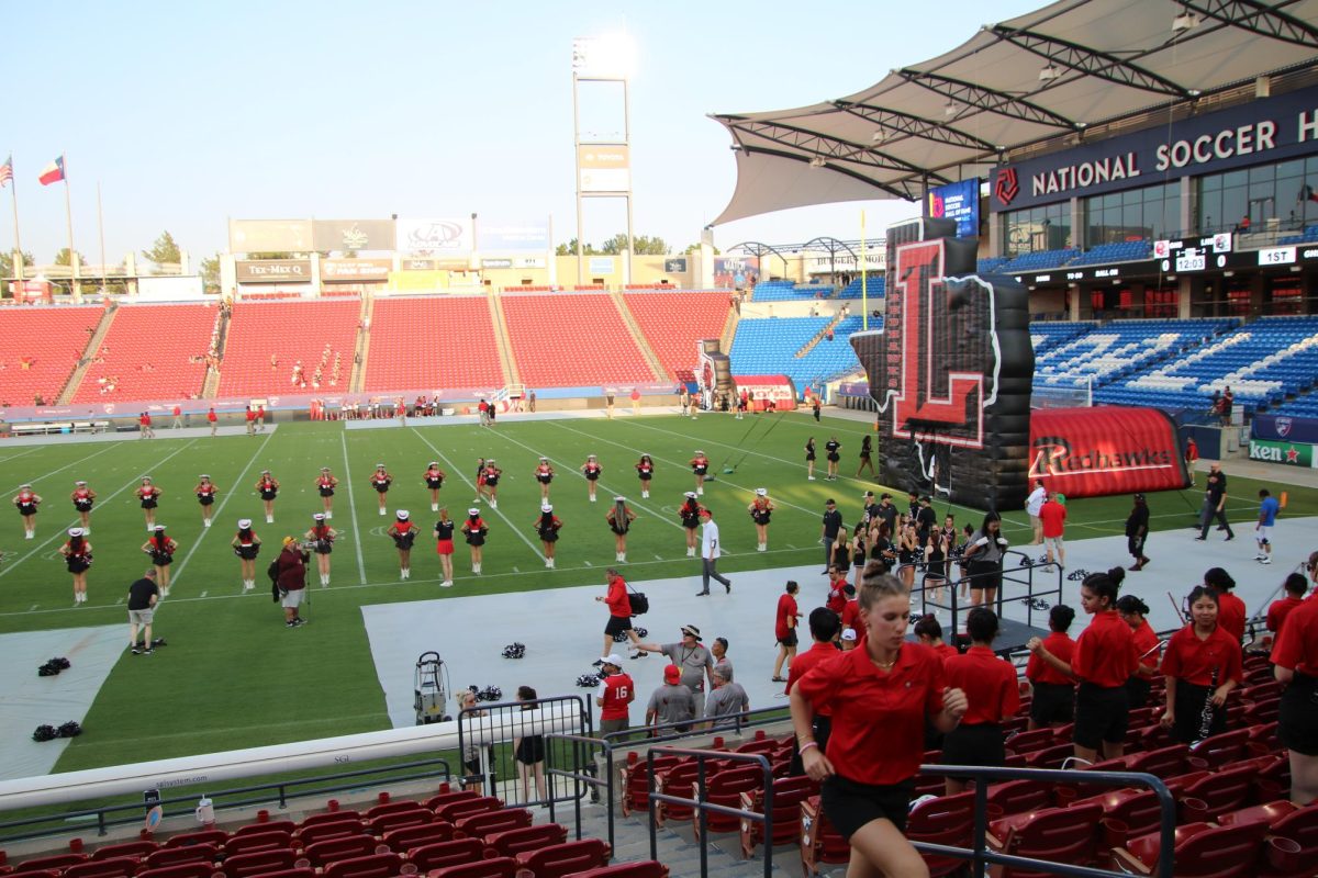 With the Soccer Hall of Fame framing one end of Toyota Stadium, and the cheerleaders and Red Rhythm on the field ready to welcome the football team, band members make final game night preparations. 