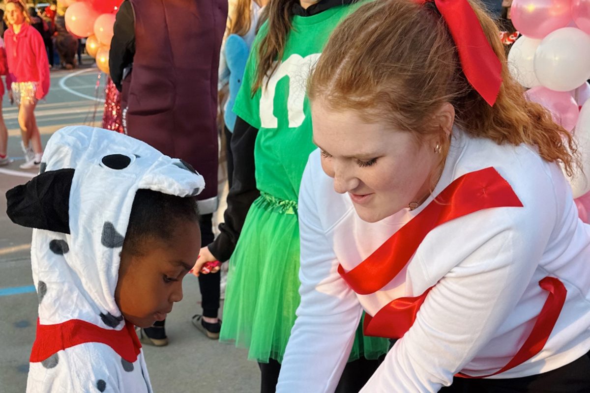 Leaning over, junior Ally Gerardot, hands candy to a little dalmation at the 2023 Trunk R Treat. The event was originally scheduled for Oct. 30 but was moved to Nov. 1 for a variety of reasons including the weather. 