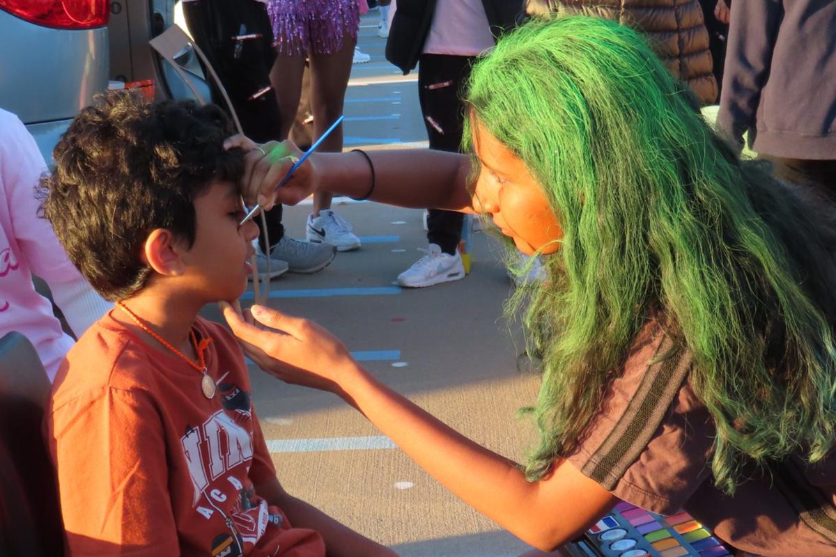 Junior Nithya Boddu forgoes her musical talents for painting at the face painting booth for orchestra. 