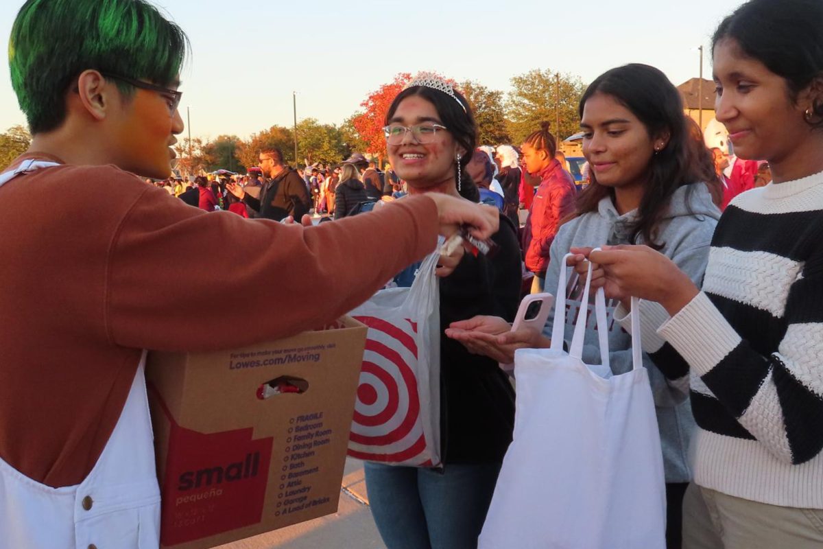 Junior Nolan Sow gives candy to juniors Riya Sharma, Tanvi Desai, and Sia Parpelli. In addition to younger kids attending Trunk R Treat, students from campus attended as well.