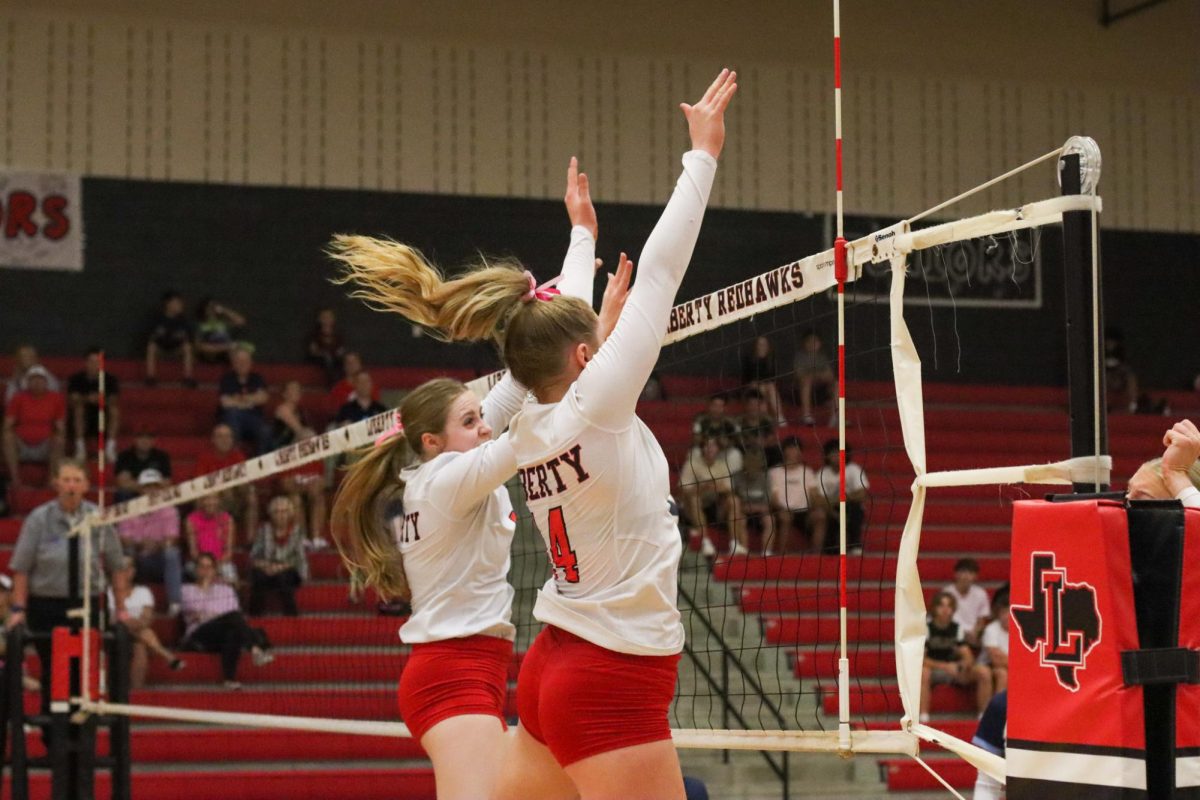 Junior Jaiden Harries and senior Mackenzie Raymond soar high as they go to block a ball by the Emerson Mavericks. They too wear pink ribbons, fighting valiantly just like breast cancer survivors and patients. 