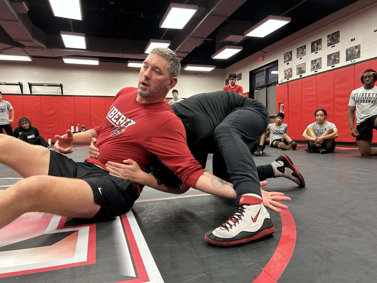 Showing the team a possible escape move, boys' head coach Justin Koons explains what to do as he shows the Redhawks wrestling team how to pull off the maneuver.